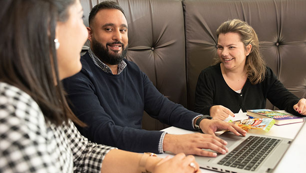 3 multicultural Mondelez staff sitting around a laptop smiling and talking.