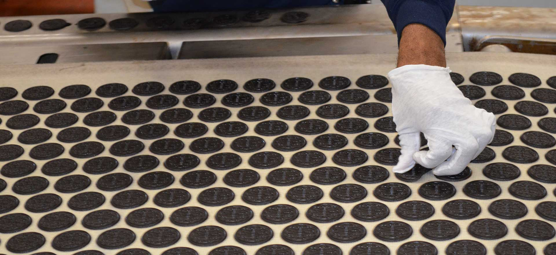 Gloved hand working on an assembly line handling Oreo cookie biscuits.