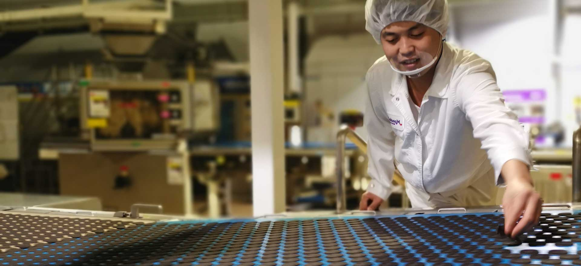 Mondelez factory worker smiling while inspecting Oreo cookies on assembly line.