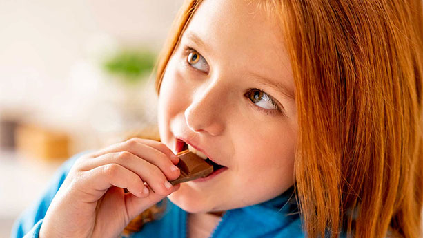 Little girl smiling while she eats a chocolate snack.