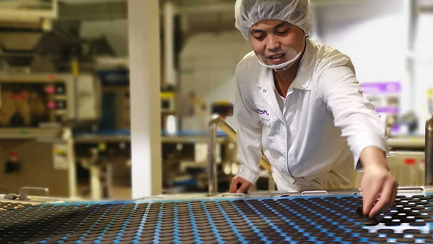 Mondelez factory worker smiling while inspecting Oreo cookies on assembly line.