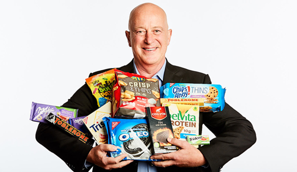 Headshot of Dirk holding a wide range of Mondelez products in his hands while he smiles.