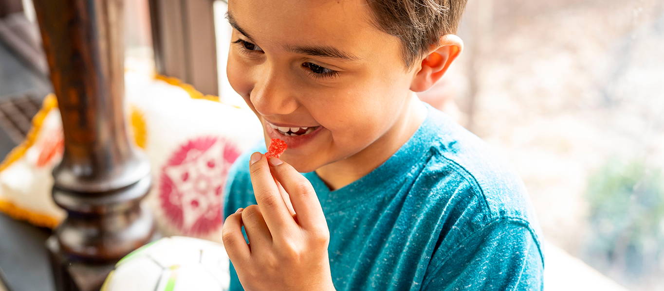 Young boy smiles while he is about to eat a sour patch kid candy.