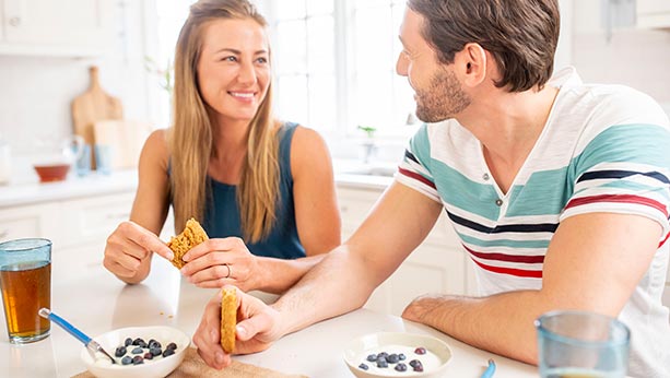 "Woman and man smiling while eating snack. "